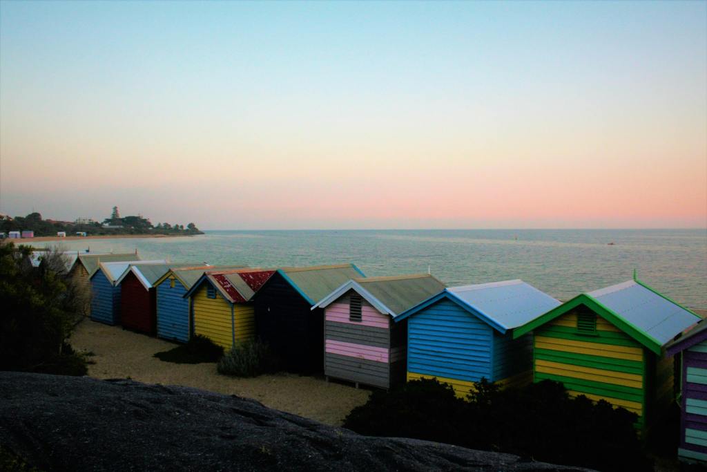 Colorful beach huts line Brighton Beach, Australia, against a serene sunset backdrop.